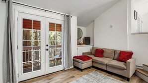 A room with a sliding glass door, a beige sofa with red cushions, a small ottoman, a white rug, and a wooden floor. - Dog-friendly Arrowhead Villas cottage with deck, fireplace & W/D- great locale (Lake Arrowhead)