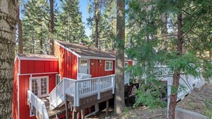 A red cabin with a white deck, surrounded by tall trees. - Dog-friendly Arrowhead Villas cottage with deck, fireplace & W/D- great locale (Lake Arrowhead)