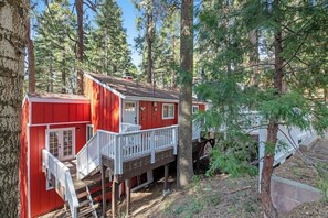 Eine rote Holzhütte mit weißer Veranda, umgeben von hohen Bäumen.
