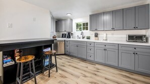 A modern kitchen with grey cabinets, a black countertop, and two stools. - Dog-friendly Arrowhead Villas cottage with deck, fireplace & W/D- great locale (Lake Arrowhead)