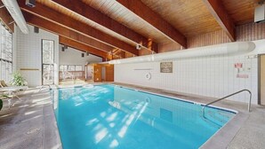 En inomhuspool med träbjälkar, kaklade väggar och ett kristallklart blått vatten.