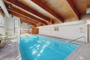 Ein Innenpool mit Holzbalken, gefliesten Wänden und klarem, blauem Wasser.