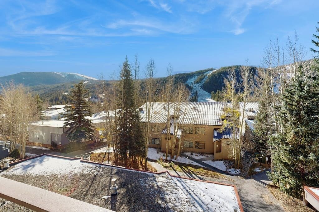 A building with a flat roof, surrounded by trees and a mountainous landscape.