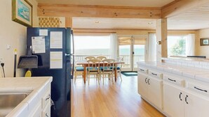 Une cuisine avec un réfrigérateur noir, des armoires en bois, une table à manger avec des chaises et une vue sur l’extérieur.