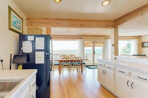 A kitchen with a black refrigerator, wooden cabinets, a dining table with chairs, and a view to the outside.