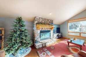 Ein Wohnzimmer mit Kamin aus Stein, einem Weihnachtsbaum und einem großen Fenster mit Aussicht.
