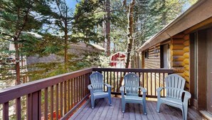 Una terraza de madera con sillas Adirondack, una cabaña de madera y árboles circundantes.