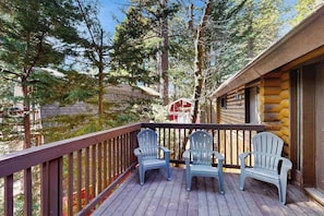 Une terrasse en bois avec des fauteuils Adirondack, un chalet en bois et des arbres tout autour.