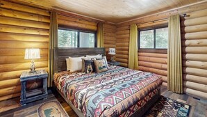 Un dormitorio tipo cabaña de madera con una cama, dos mesitas de noche y una ventana con cortinas.
