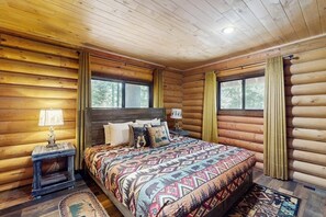 Une chambre à coucher située dans une cabane en rondins, avec un lit, deux tables de chevet et une fenêtre avec des rideaux.