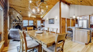 Un comedor amplio con mesa y sillas de madera, una chimenea de piedra y una cocina con armarios de madera y una isla central.