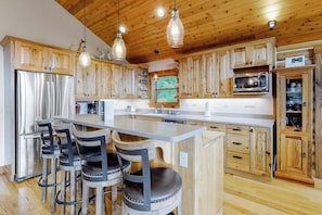 Eine Küche mit Holzausstattung, einem Edelstahlkühlschrank, einer Mikrowelle und einer Bar mit Sitzgelegenheiten.