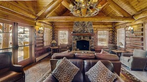 A log cabin interior with a fireplace, leather sofas, and a chandelier.