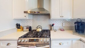 Een keuken met witte kasten, een roestvrijstalen afzuigkap, een gasfornuis, een waterkoker en een koffiezetapparaat.