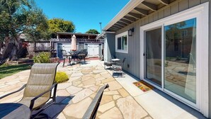 Een terras met stenen vloer, tuinmeubilair en een schuifdeur naar een overdekt gedeelte.