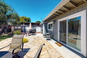 Eine Terrasse mit Steinbelag, Gartenmöbeln und einer Glastür zu einem überdachten Bereich.