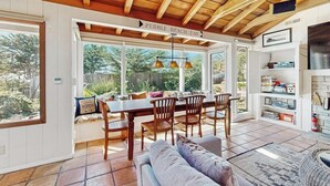 A dining area with a wooden table and chairs, a sofa, and a view of the outdoors. - Surf-side monthly rental with ocean views, beach access & private hot tub (Carmel-by-the-Sea)