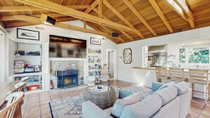 A spacious living area with a fireplace, a sofa, a dining table, and a kitchen in the background. - Surf-side monthly rental with ocean views, beach access & private hot tub (Carmel-by-the-Sea)