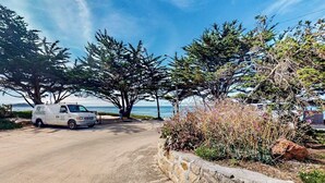 A white van parked on a dirt road, surrounded by trees and a stone wall. - Surf-side monthly rental with ocean views, beach access & private hot tub (Carmel-by-the-Sea)