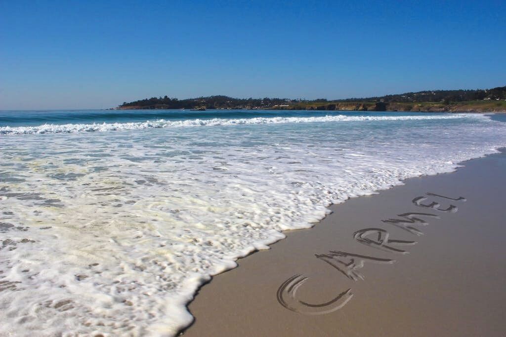 Ein Strand, auf dem das Wort 'CARMEL' im Sand geschrieben steht.