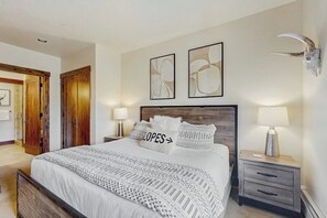 A bedroom with a bed, two wall-mounted lamps, a wooden headboard, and a mounted animal skull. - Cozy mountain condo with ski-in access, hot tub & stunning views (Breckenridge)