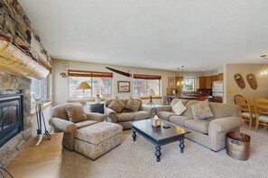 A living room with a fireplace, two sofas, a coffee table, and a kitchen in the background. - Cozy mountain condo with ski-in access, hot tub & stunning views (Breckenridge)