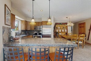 A kitchen with granite countertops, stainless steel appliances, wooden cabinets, and a dining area with a wooden table and chairs. - Cozy mountain condo with ski-in access, hot tub & stunning views (Breckenridge)