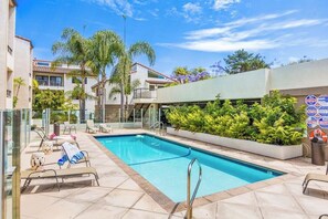 A swimming pool with lounge chairs, palm trees, and a building with a balcony. - Ocean-view condo in Santa Barbara steps to beach with pool & balcony (Santa Barbara)