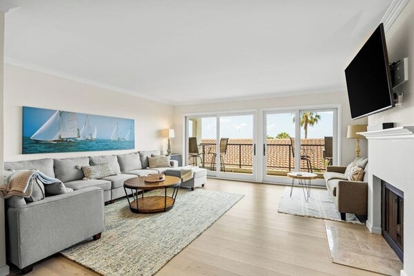 A living room with a sofa set, a coffee table, a fireplace, and a TV mounted on the wall. - Ocean-view condo in Santa Barbara steps to beach with pool & balcony (Santa Barbara)