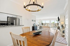 A modern kitchen with stainless steel appliances, a wooden dining table with chairs, and a chandelier. - Ocean-view condo in Santa Barbara steps to beach with pool & balcony (Santa Barbara)
