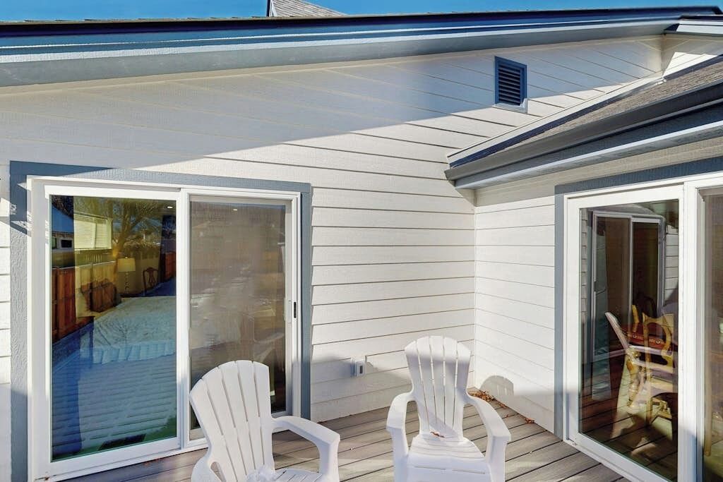 Un espace extérieur abrité comprenant deux fauteuils Adirondack blancs, une porte-fenêtre coulissante et une terrasse en bois.
