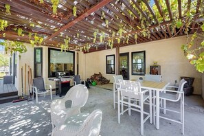 Une terrasse extérieure avec des meubles en osier blanc, une pergola couverte de plantes grimpantes et un espace barbecue.