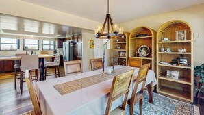 Comedor con una mesa dispuesta para cuatro, una araña y una cocina al fondo.