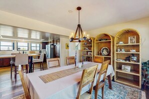 Un coin repas avec une table dressée pour quatre personnes, un lustre et une cuisine en arrière-plan.