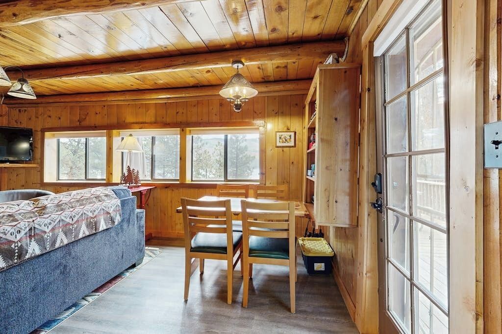 A wooden cabin interior with a sofa, dining table, chairs, and a TV.