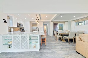 A modern kitchen with a central island, a dining area with a wooden table and chairs, and a living area with a sofa. - 2-Story Newly Remodeled Home w/Private Patio, Great Location, Fireplace, WiFi (Newport Beach)