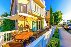 A balcony with a table and chairs, a white railing, and a view of parked cars and greenery. - 2-Story Newly Remodeled Home w/Private Patio, Great Location, Fireplace, WiFi (Newport Beach)