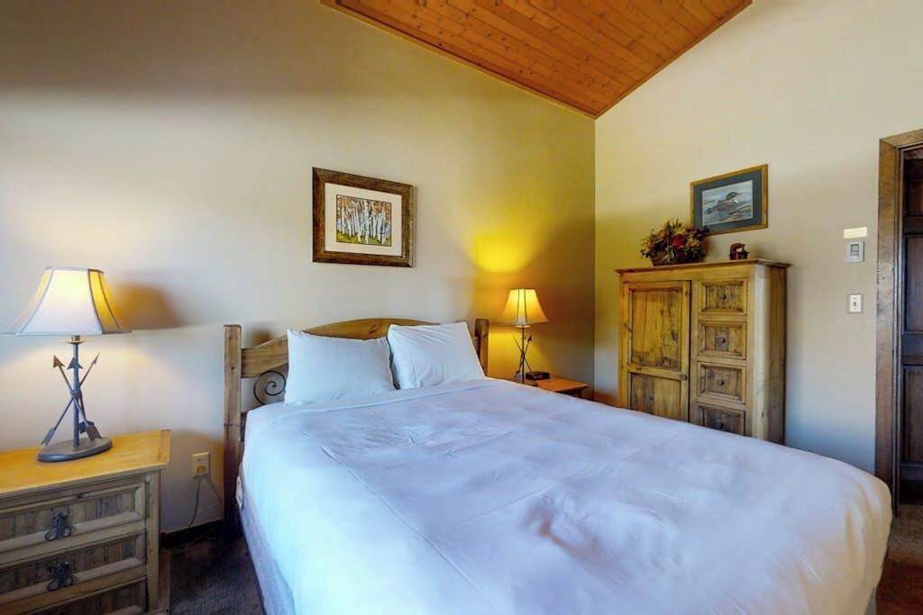 Une chambre à coucher avec un grand lit, deux lampes de chevet, une tête de lit en bois, une table de chevet, une commode et deux tableaux encadrés accrochés au mur.