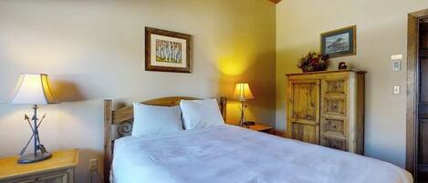 Une chambre à coucher avec un grand lit, deux lampes de chevet, une tête de lit en bois, une table de chevet, une commode et deux tableaux encadrés accrochés au mur.