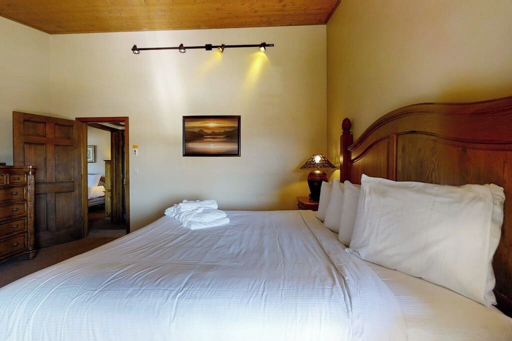 Ein Schlafzimmer mit einem Holz-Kopfteil, einem Bett mit weißen Leinen, einer Nachttischlampe und einem gerahmten Bild an der Wand.