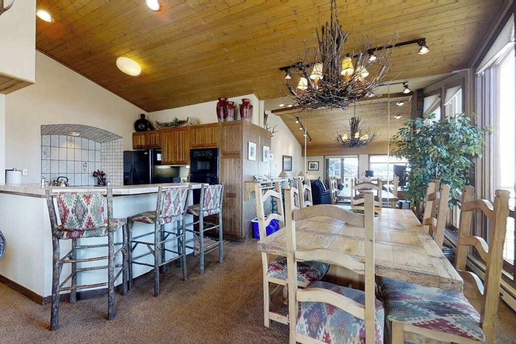 A spacious kitchen with wooden cabinets, a central island with bar stools, and a dining area with a long table and chairs.
