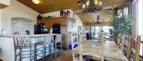 A spacious kitchen with wooden cabinets, a central island with bar stools, and a dining area with a long table and chairs.
