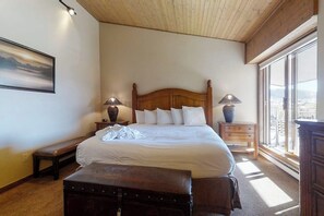 Ein Schlafzimmer mit einem großen Bett, zwei Nachttischlampen, einer Bank, einem Koffer und einem Fenster mit Blick.