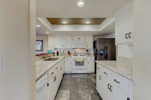 Eine moderne Küche mit weißen Schränken, einer Arbeitsplatte aus Granit, einer eingebauten Mikrowelle und einem Edelstahl-Kühlschrank.