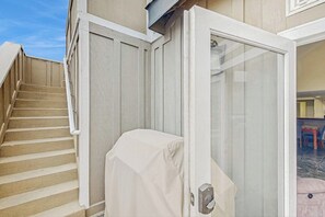 Eine überdachte Außentreppe führt zu einer Glastür, einer überdachten Terrassenfläche und bietet einen Blick in einen Innenraum mit gefliestem Boden.