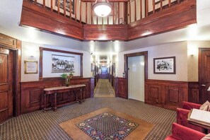 A grand hallway with wooden paneling, a central rug, and framed pictures on the walls.