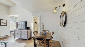 Ein Essbereich mit Holztisch und -stühlen, einem Fernseher auf einem Schrank und einer Wandlampe.