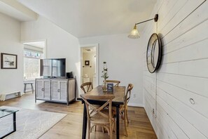 A dining area with a wooden table and chairs, a television on a cabinet, and a wall-mounted lamp.