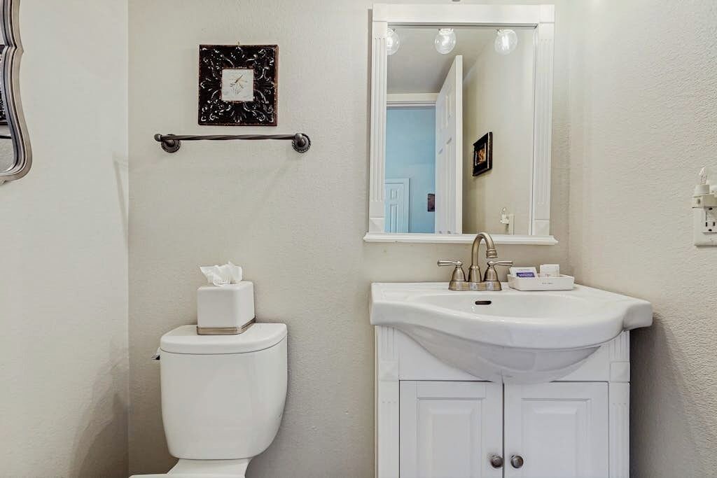 A bathroom with a toilet, sink, mirror, and a picture frame on the wall.