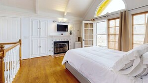 Quarto com lareira, uma cama grande, uma televisão montada acima e uma janela com cortinas.